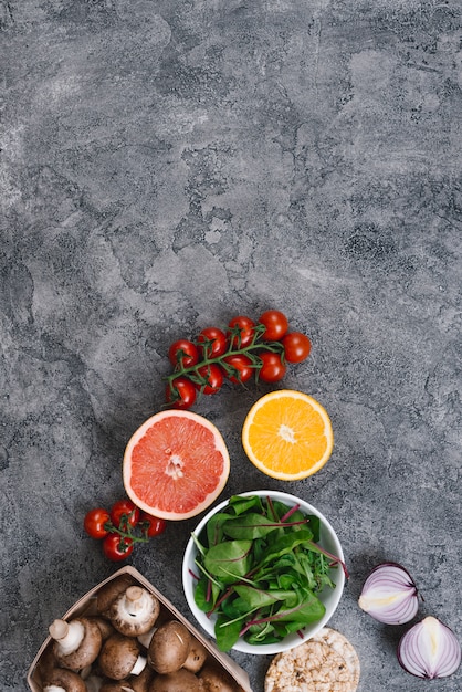 Free photo cherry tomatoes; halved citrus fruit; spinach; mushrooms; onion and rice puffed cake on concrete backdrop