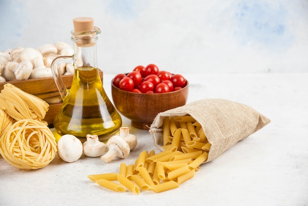 Cherry tomatoes with olive oil, mushrooms and raw pastas on the marble.