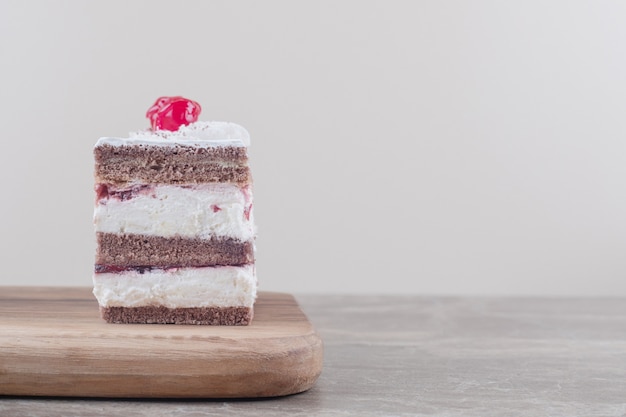 Free photo cherry topped cake slice on a board on marble