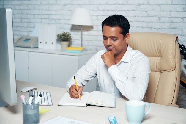 Chest-up shot of white-collar worker sitting at the office desk and taking notes