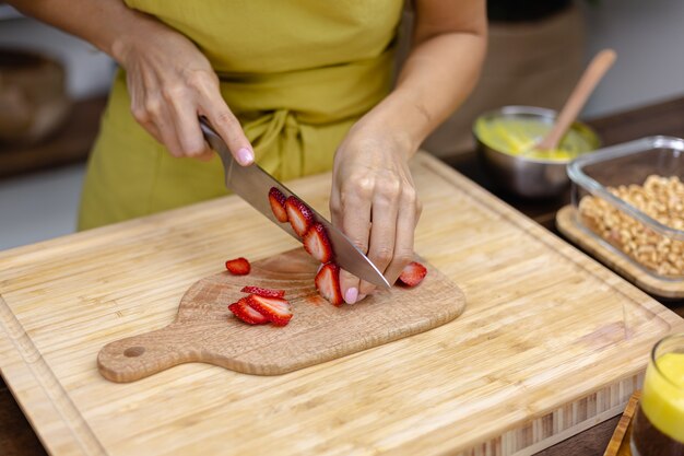 Chia pudding making process. Woman cut strawberry on wooden board.