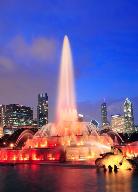 Chicago skyline with skyscrapers and Buckingham fountain in Grant Park at dusk lit by colorful lights.