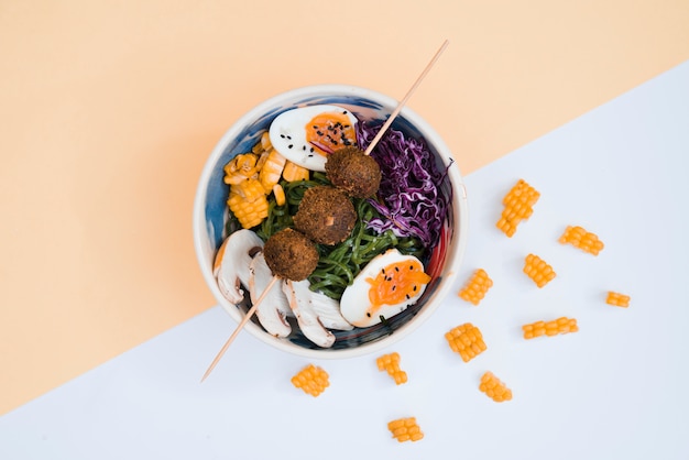 Free photo chicken balls in stick over the bowl with salad and eggs on dual background