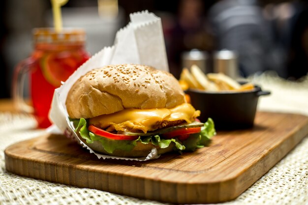 Chicken burger ob wooden board lettuce cheese tomato cucumber side view