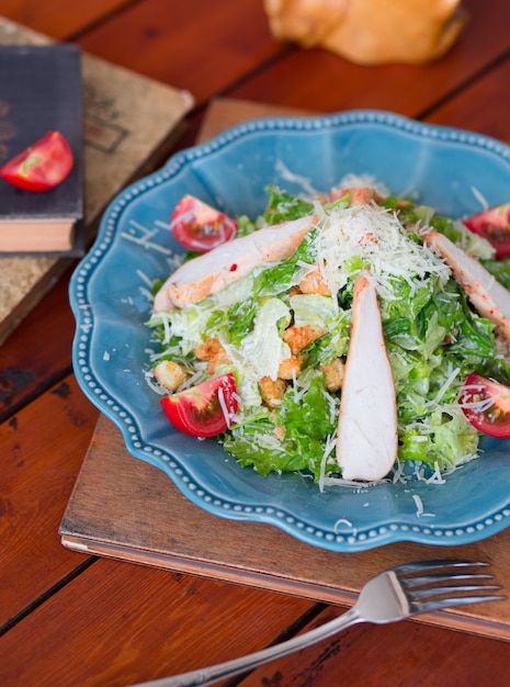 Chicken caesar salad with chopped parmesan cheese fresh lettuce and tomatoes, crackers in blue plate   