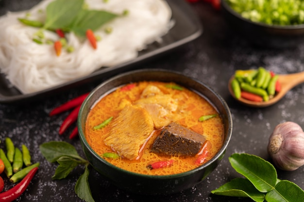 Chicken curry in a black cup with rice noodles.