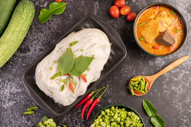 Chicken curry in a black cup with rice noodles.