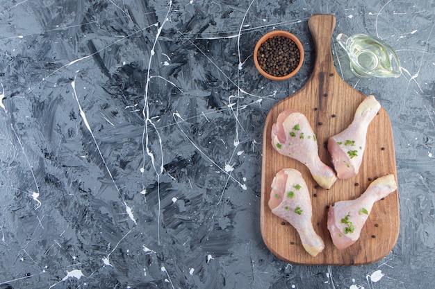 Free photo chicken drumsticks on a cutting board next to oil and spice bowls , on the blue background.