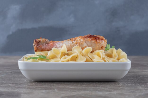 Chicken drumsticks over pasta in the bowl , on the marble surface.