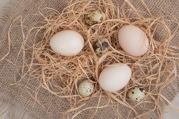 Chicken egg with quail eggs and hay on sackcloth .