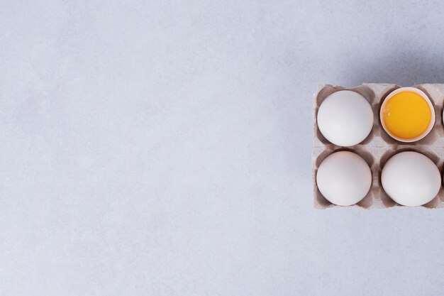 Chicken eggs in paper container on white surface.