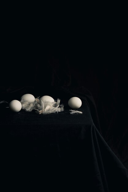 Chicken eggs with feathers on edge of table between blackness