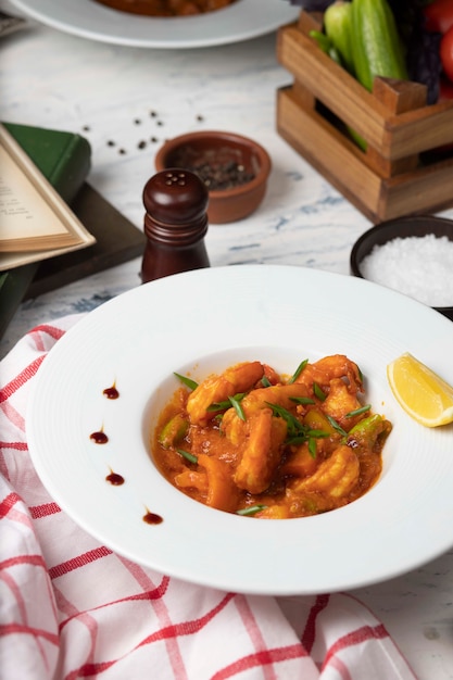 Chicken feet stew in tomato sauce in white bowl with vegetables and lemon. 