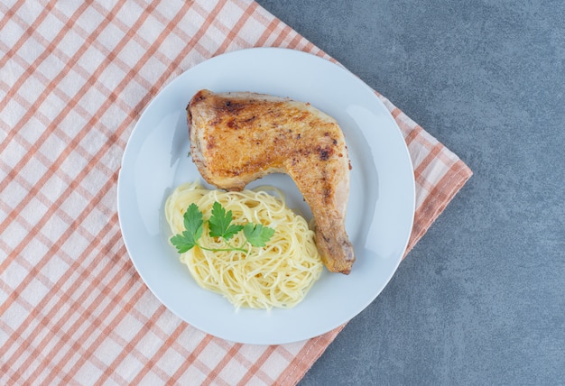 Chicken leg and spaghetti on white plate.