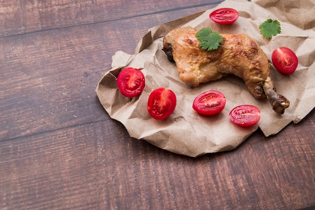 Free photo chicken legs on brown paper with halved tomatoes on wooden table