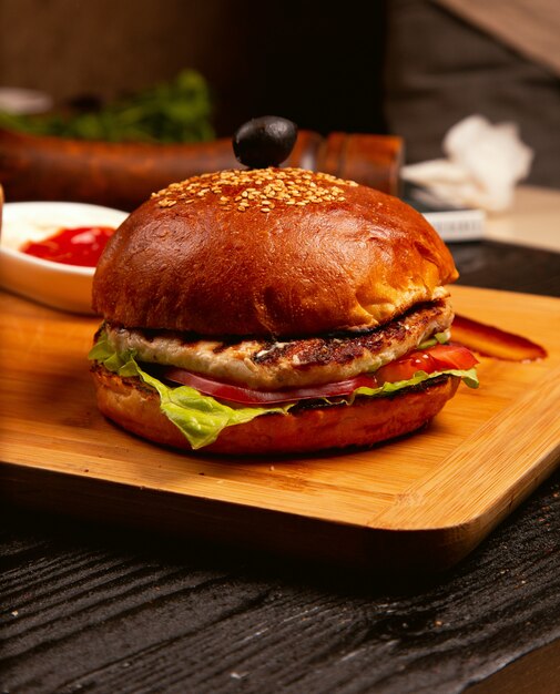 Chicken meat burger with tomato slices and lettuce served with ketchup and mayonnaise on wooden board. 