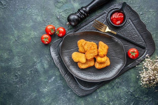 Free Photo chicken nuggets on a black plate and elegant fork ketchup on dark tray white flower tomatoes