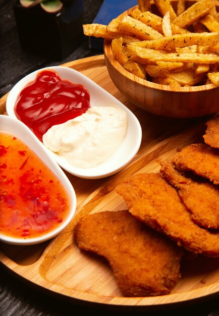 Chicken nuggets served with french fries, ketchup and mayonnaise on wooden board