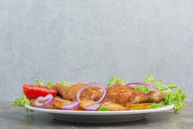 Chicken nuggets with fried potato and onion on white plate .