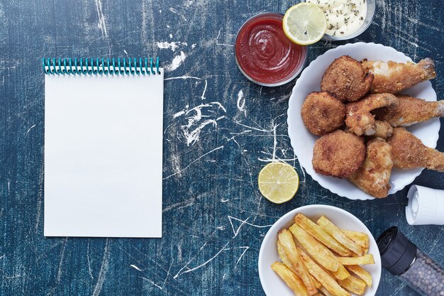 Chicken nuggets with potatoes and sauces with a notebook aside.