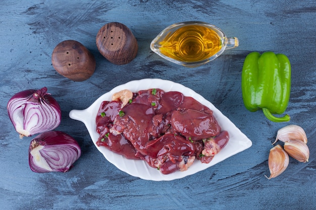 Chicken offal on a platter, oil bowl, salt onion, garlic and pepper on the blue surface