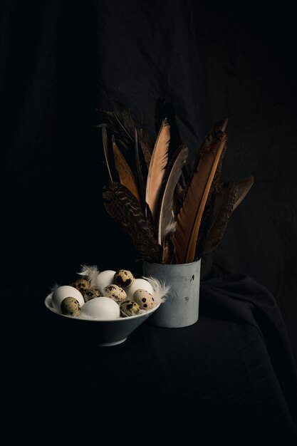 Chicken and quail eggs between feathers in bowl near big quills in can