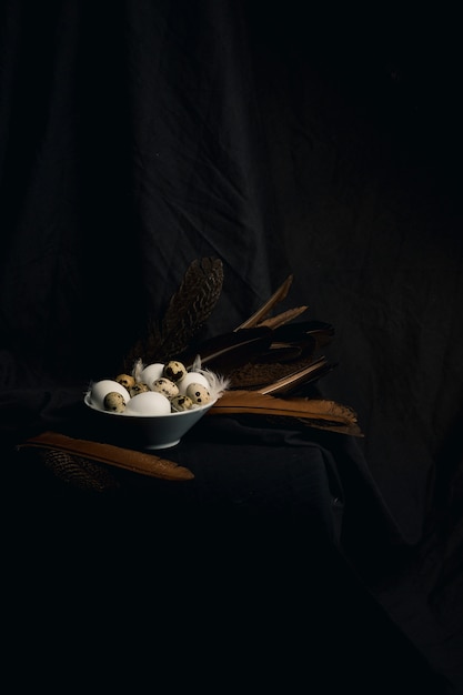 Free Photo chicken and quail eggs between feathers in bowl near big quills