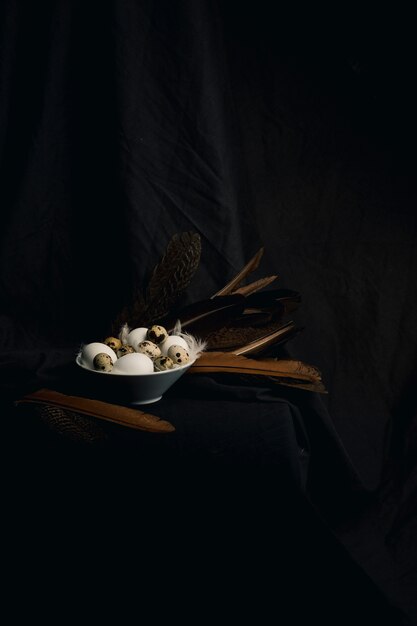 Chicken and quail eggs between feathers in bowl near big quills