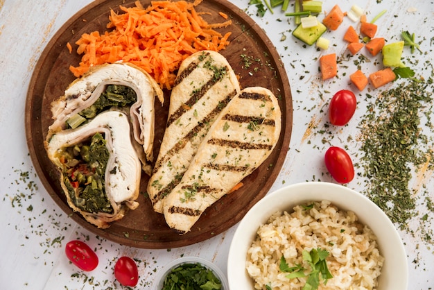 Free photo chicken roll and breast on wooden plate arranged with vegetable pieces