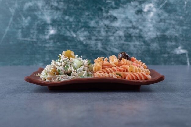 Chicken salad and fusilli pasta on brown plate.