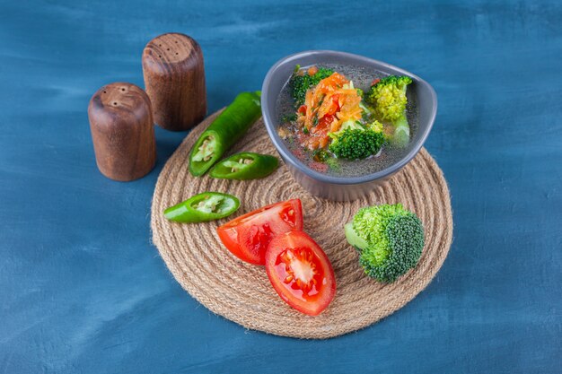 Chicken soup in a bowl and sliced vegetables on a trivet on the blue surface