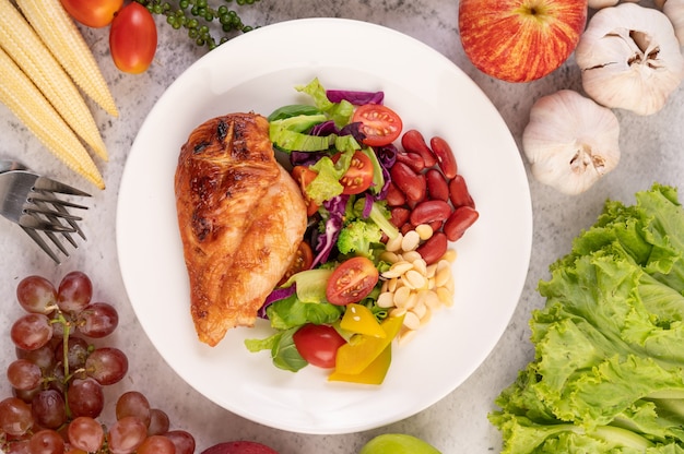 Free photo chicken steak topped with white sesame, peas, tomatoes, broccoli and pumpkin in a white plate.