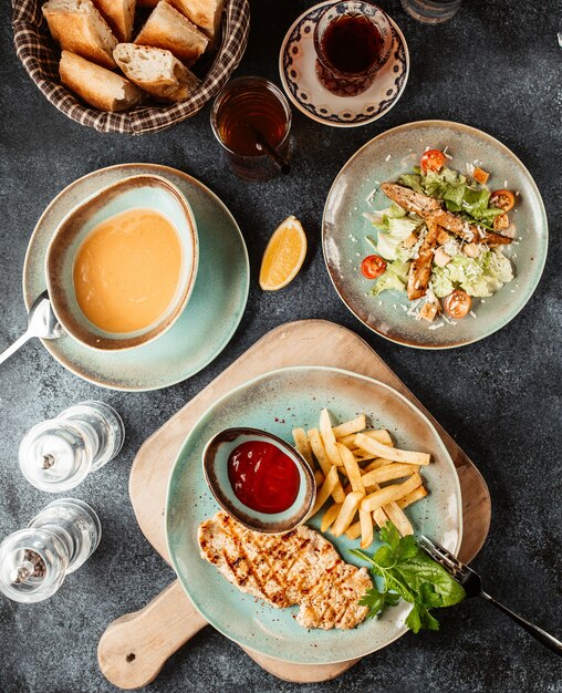 Chicken steak with french fries and ketchup served with soup and caesar salad