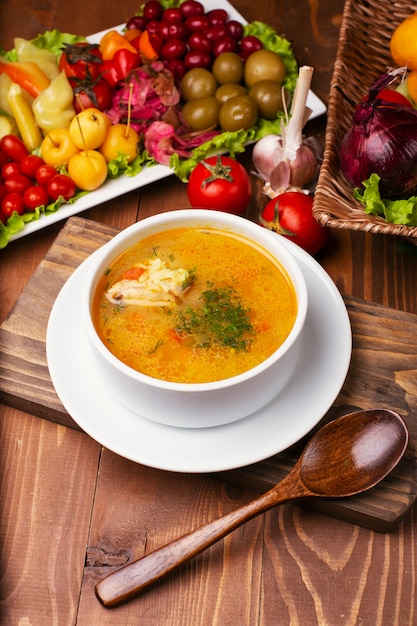 Free Photo chicket soup with a piece of meat in tomato sauce. copped parsley, in white bowl decorated with turshu on wooden table.