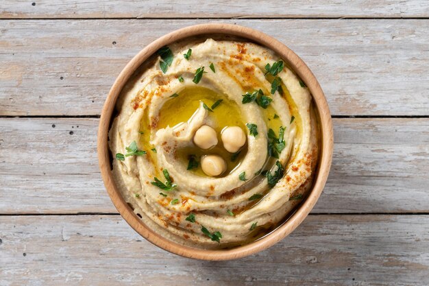 Chickpea hummus in a wooden bowl garnished with parsley paprika and olive oil on wooden table