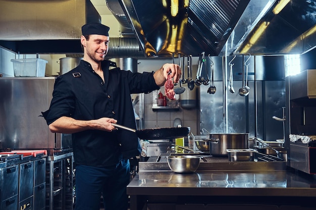 Free photo the chief cook holds pork meat under the fry pan in a kitchen.