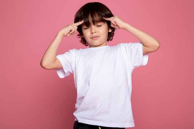 Free photo child boy cute adorable portrait in white t-shirt and black trousers on pink desk