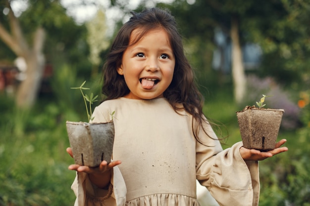 Free photo child girl holding a seedlings ready to be planted in the ground. little gardener in a brown dress.