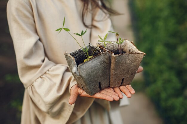 Child girl holding a seedlings ready to be planted in the ground. Little gardener in a brown dress.