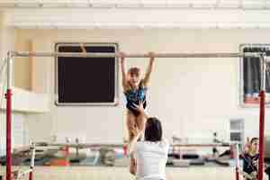 Free photo child gymnastics balance beam.  girl gymnast athlete during an exercise horizontal bar in gymnastics competitions. coach with child.