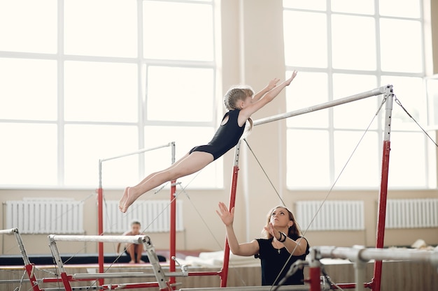 Free Photo child gymnastics balance beam.  girl gymnast athlete during an exercise horizontal bar in gymnastics competitions. coach with child.