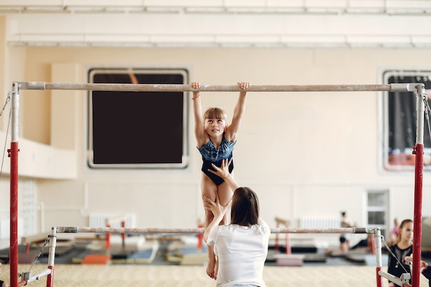 Child gymnastics balance beam.  Girl gymnast athlete during an exercise horizontal bar in gymnastics competitions. Coach with child.