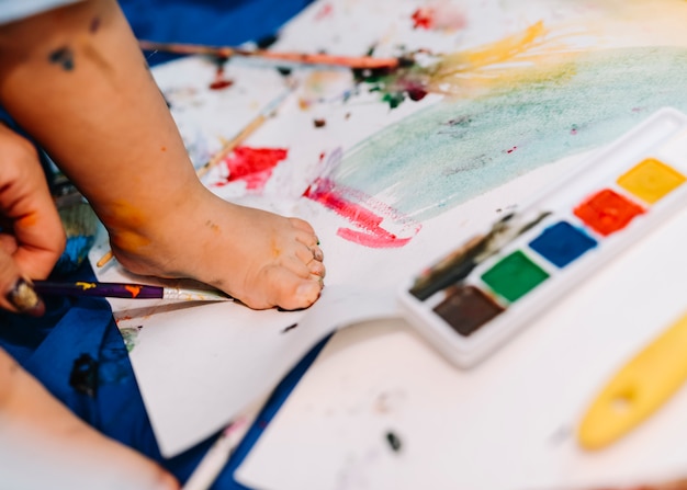 Free photo child leg on paper near water colors