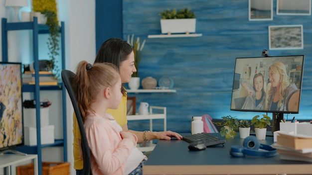 Child and parent talking to adult and girl on video call at desk. Mother and daughter feeling cheerful, bonding with friends on online conference for remote chatting on internet connection.