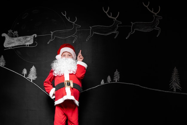 Free photo child in santa claus costume pointing at background