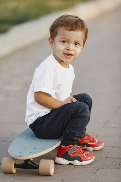 Child in a summer park. Boy in a white t-shirt. Kid with skate.