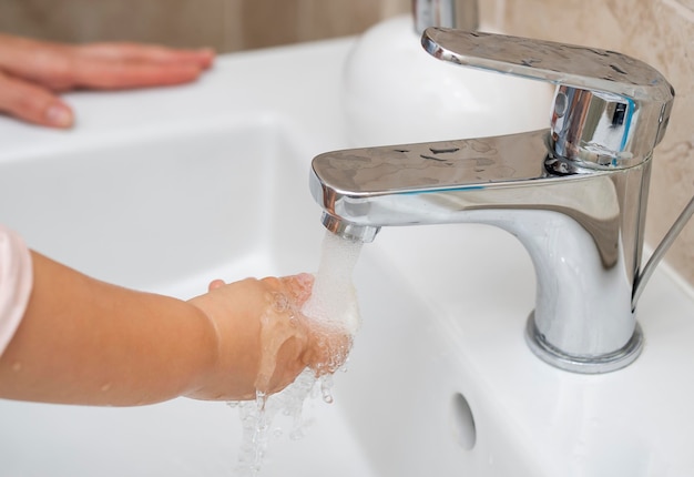 Child washing their hands at home with mom's help