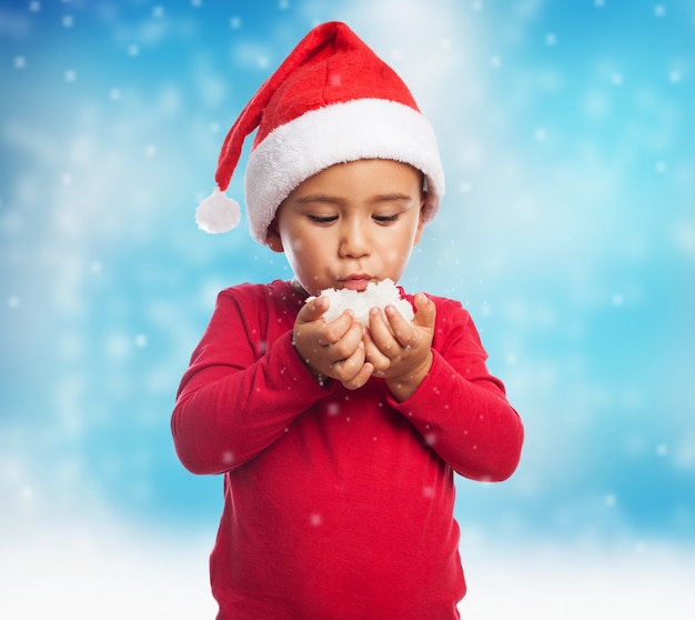 Child wearing santa hat and blowing snow from his hands