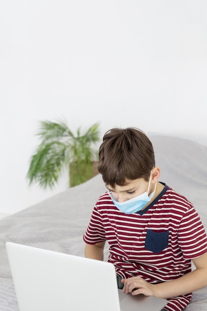 Child with medical mask looking at laptop