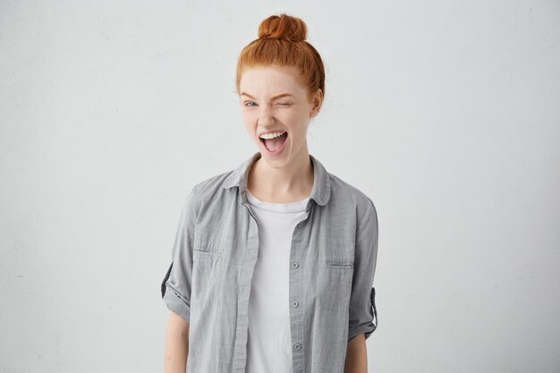 Childish and playful red haired teenage girl winking, keeping mouth wide opened